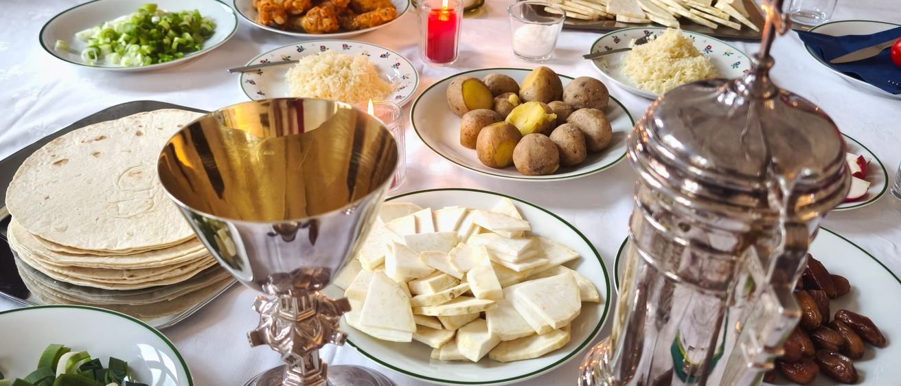 Ein Tisch ist mit einer Auswahl an Gerichten gedeckt, darunter eine Suppenschüssel, Salate, Brot und verschiedene Gemüsesorten, begleitet von Kerzen und Silberbesteck.