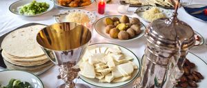 Ein Tisch ist mit einer Auswahl an Gerichten gedeckt, darunter eine Suppenschüssel, Salate, Brot und verschiedene Gemüsesorten, begleitet von Kerzen und Silberbesteck.