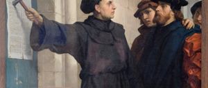 Ein Gemälde zeigt einen Mann in einer schwarzen Robe, der zeigt, neben zwei bärtigen Männern in Hüten, einer in einem braunen Mantel, vor einer Steinmauer.