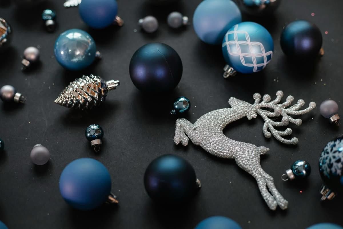 Eine Sammlung von blauen Weihnachtskugeln, darunter ein Kiefernzapfen-Ornament, ein Rentier-Ornament und verschiedene kugelförmige Ornamente, angeordnet auf einer dunklen Oberfläche.