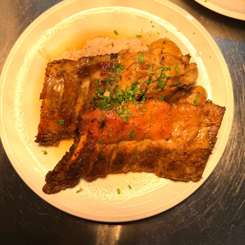 Ein Teller mit gegrillten Rippchen mit Sauce und Kräutern, begleitet von Reis, wird auf einer Metalloberfläche serviert.