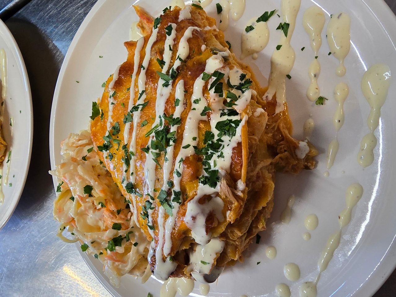 Ein weißer Teller mit einer Portion Käse-Enchiladas, bedeckt mit weißer Sauce und mit grünen Kräutern garniert.