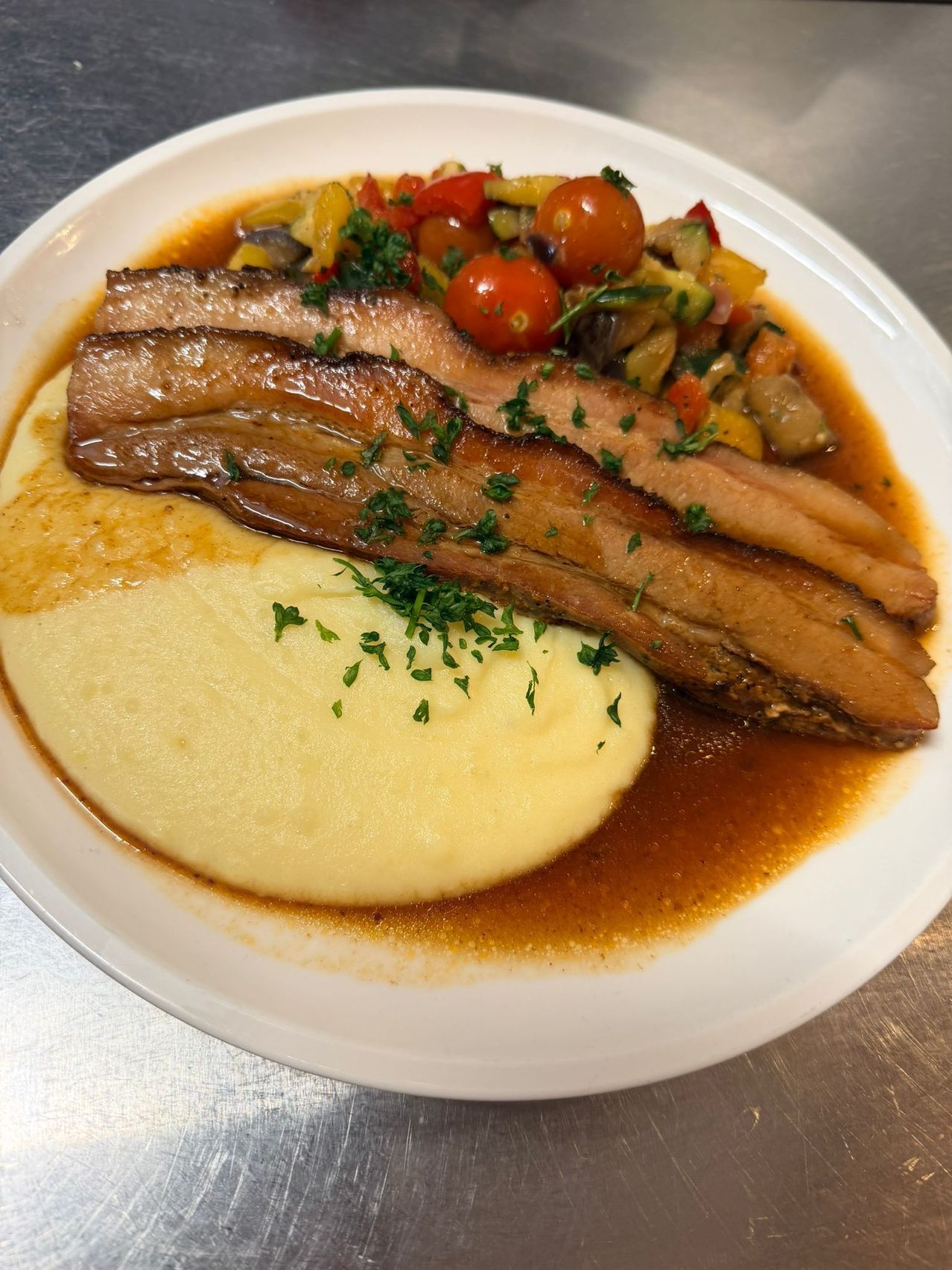 A plate with braised pork on a bed of creamy polenta, topped with a medley of colorful vegetables.