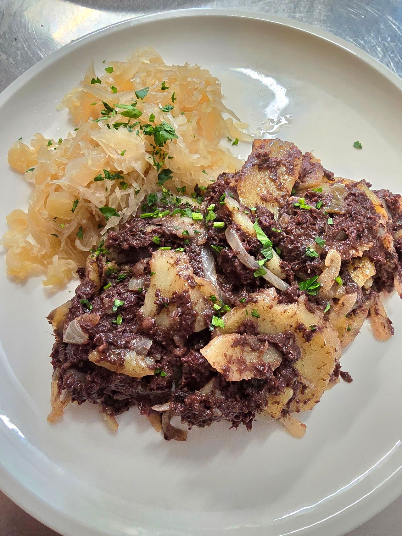 Ein Teller mit einer Blutwurst und Sauerkraut, mit Kräutern garniert, serviert mit Kartoffelpüree.
