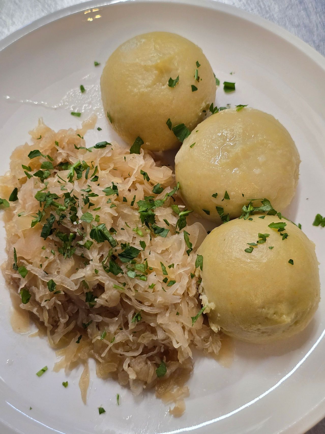A plate with three dumplings and a side of sauerkraut garnished with parsley.