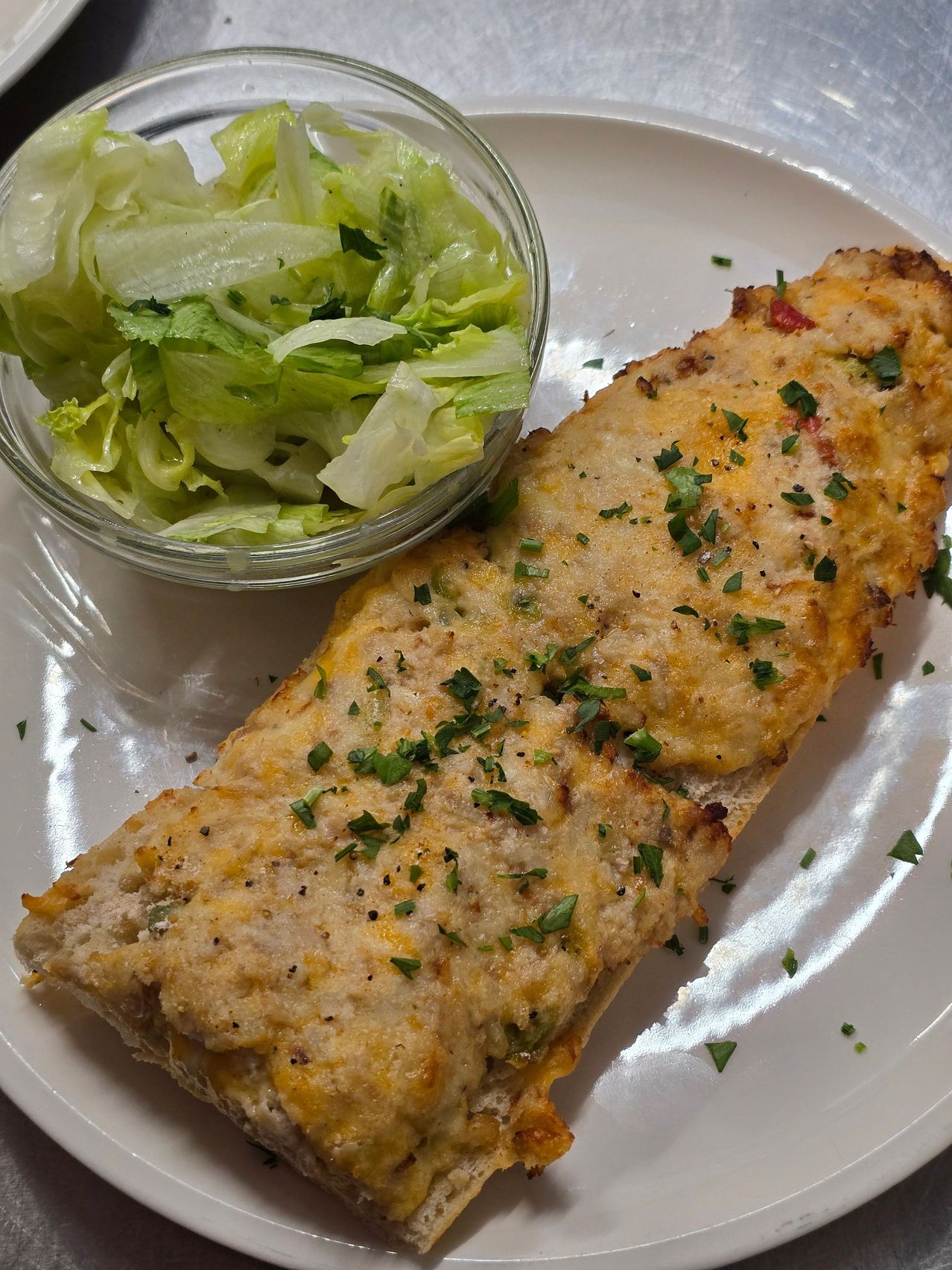 Ein Nahaufnahme eines käsigen, panierten Hähnchenbrustsandwiches mit einer Beilage von grünem Salat auf einem weißen Teller.