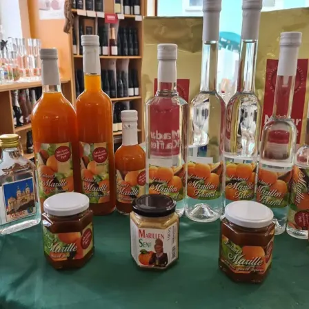 Ein Tisch zeigt verschiedene Marille-Produkte, darunter Flaschen mit Likör, Marmelade und eine kleine Flasche Likör. Die Flaschen sind mit dem Markennamen Marille beschriftet.