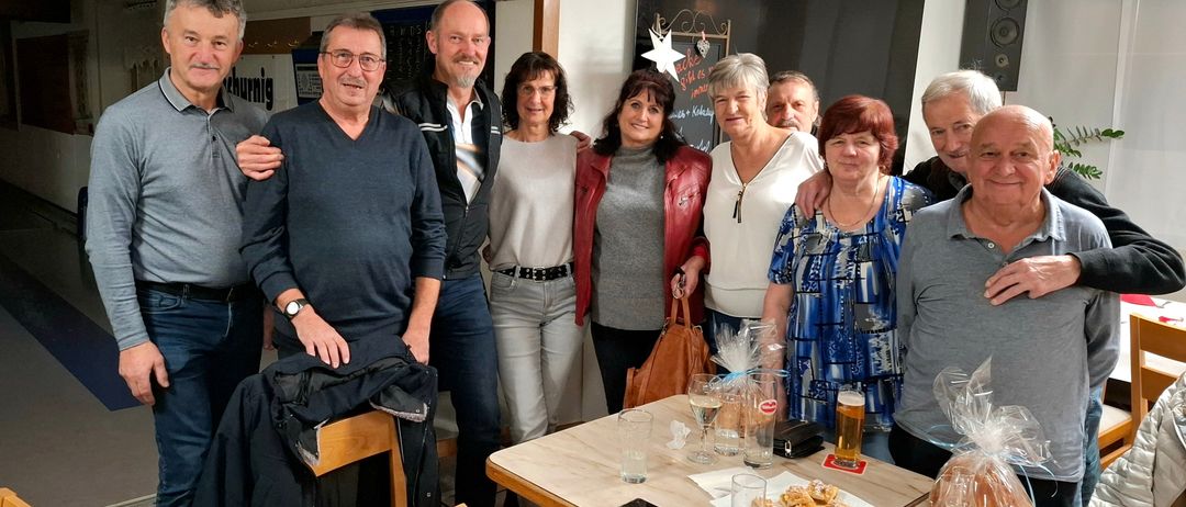 Gruppe von Menschen, die zusammenstehen, lächeln und für ein Foto in einem Raum posieren, in dem ein Tisch voller Getränke und Snacks steht.