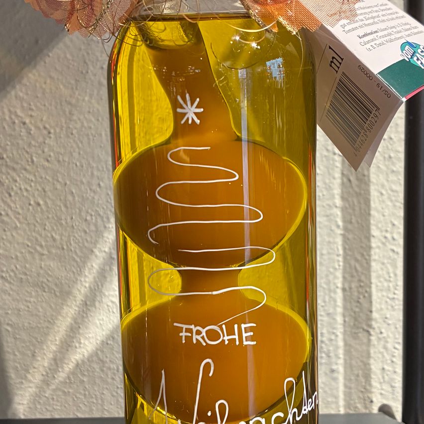 Eine Flasche mit goldener Flüssigkeit mit festlichem Design und dem Wort Frohe darauf. Die Flasche hat ein dekoratives Band obenauf.