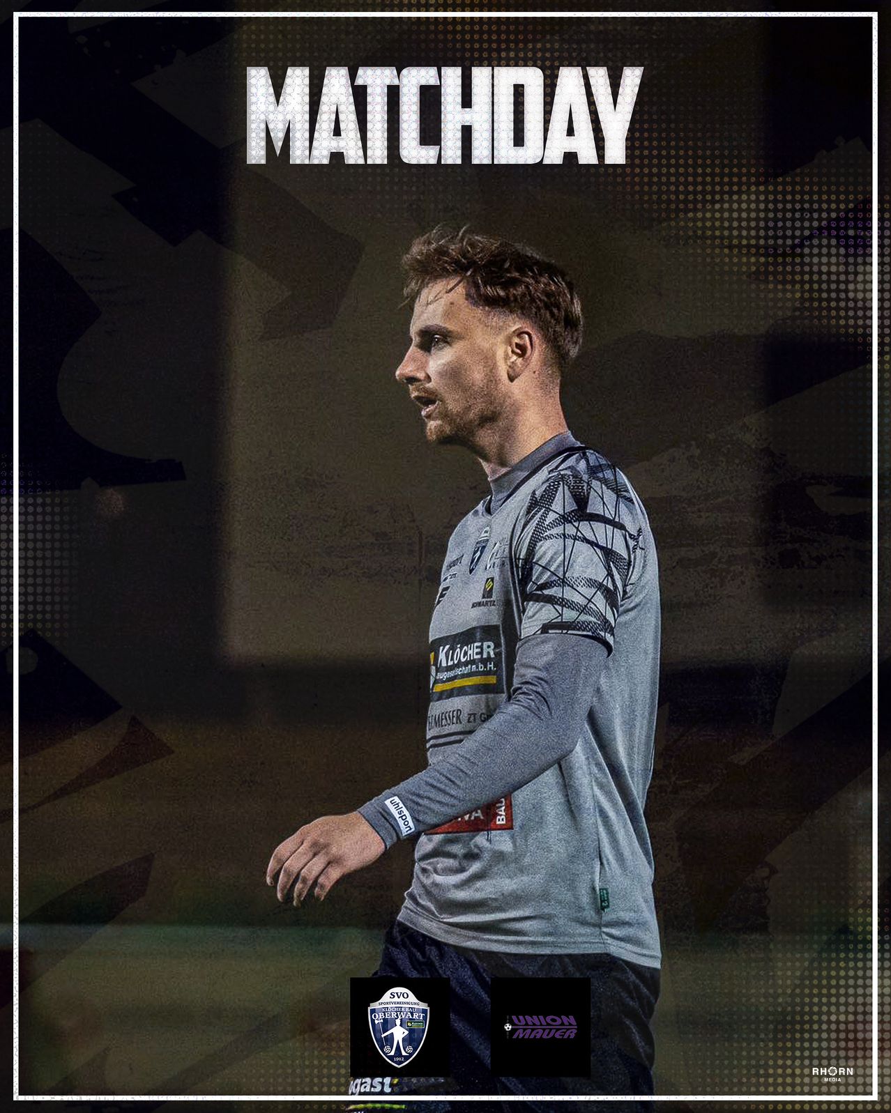 Ein Fußballspieler in einem grauen Trikot mit 'Klocher' und 'Heimtextil' Logos auf der Vorderseite steht mit ernstem Gesichtsausdruck.