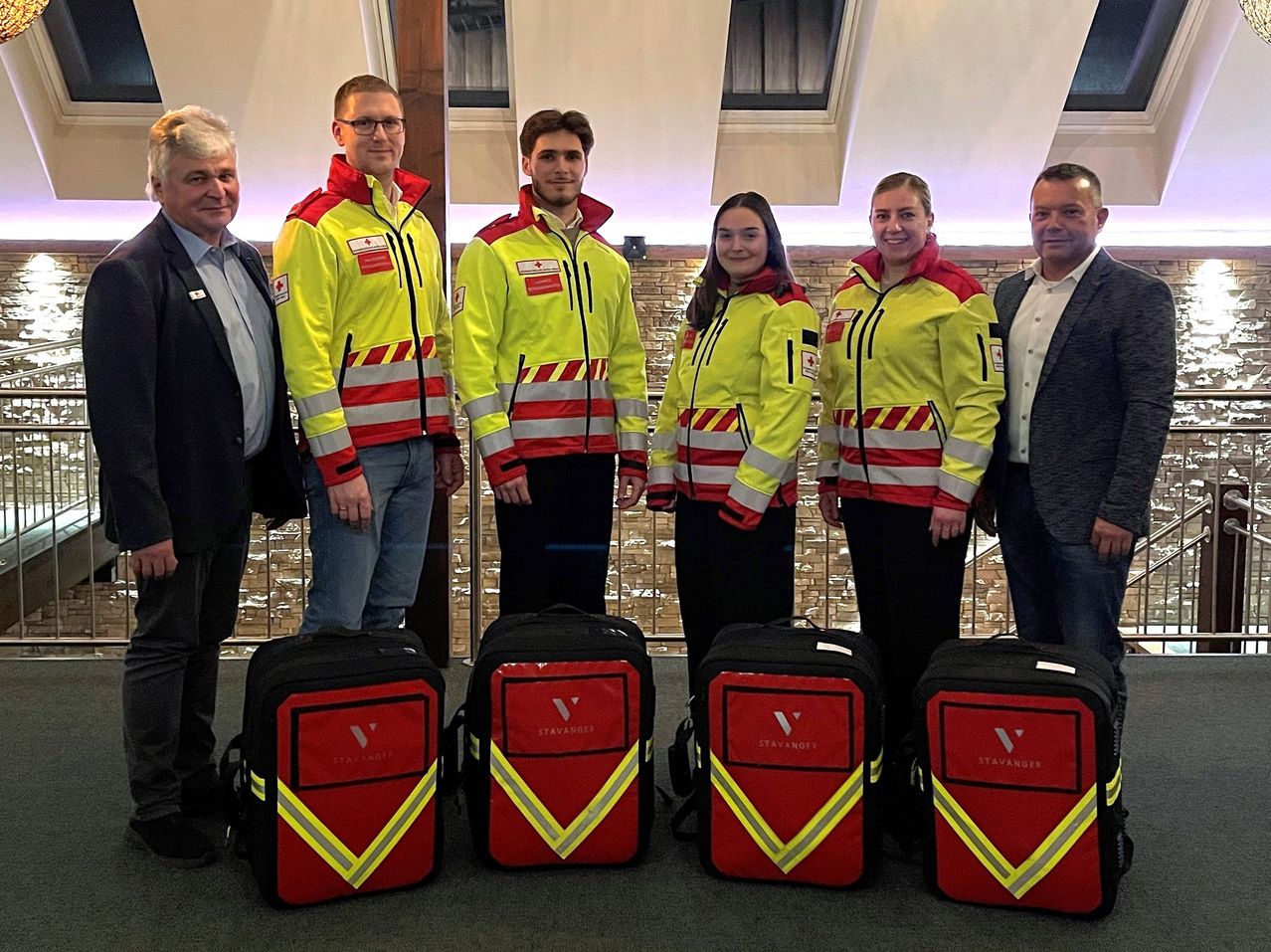 Fünf Personen in gelben und roten Warnwesten stehen mit Rucksäcken mit der Aufschrift Stavanger. Zwei Männer und drei Frauen, sie lächeln und posieren für ein Foto.