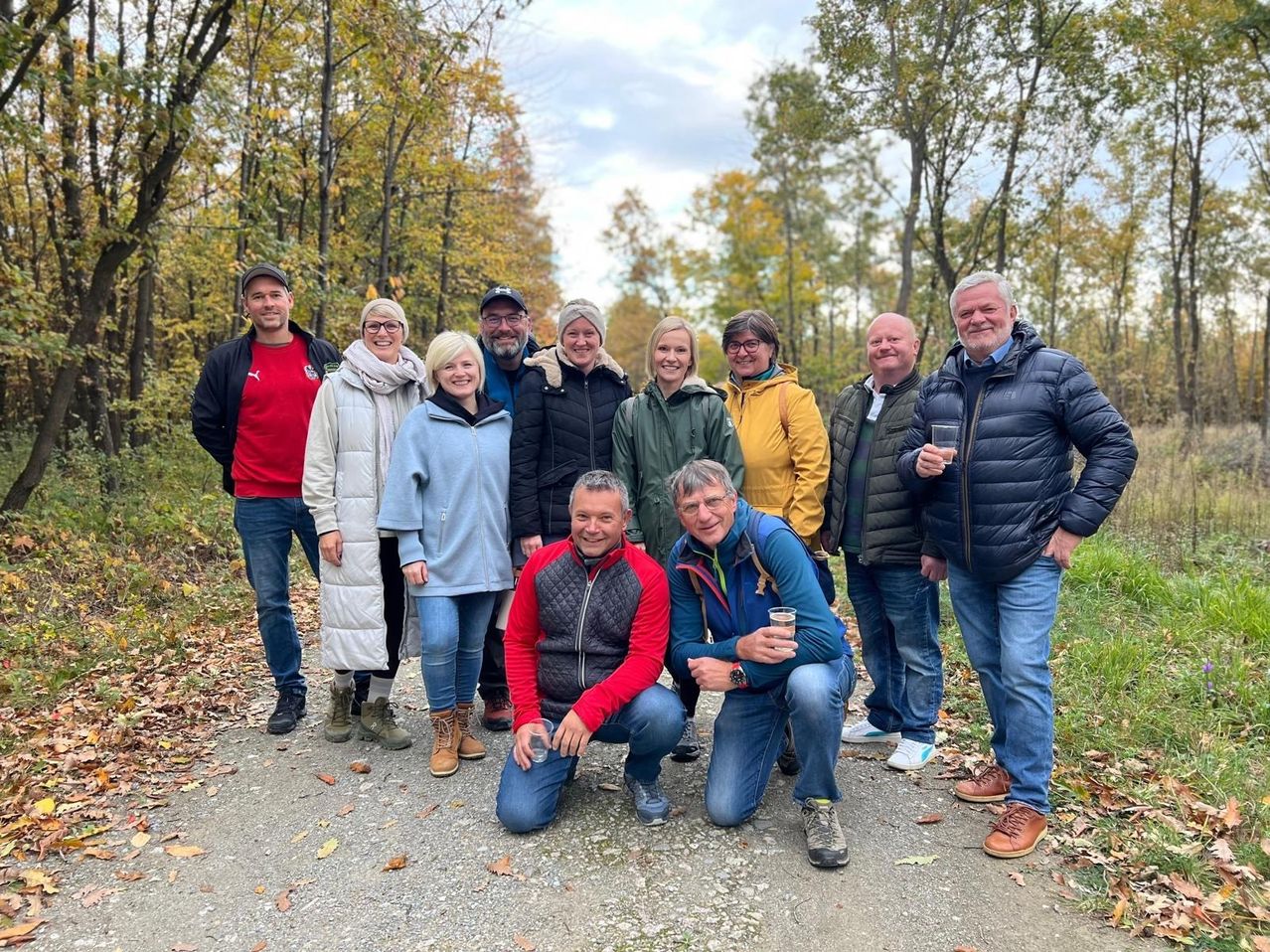 Eine Gruppe von Menschen in Winterkleidung posiert für ein Foto auf einem von Bäumen gesäumten Pfad.
