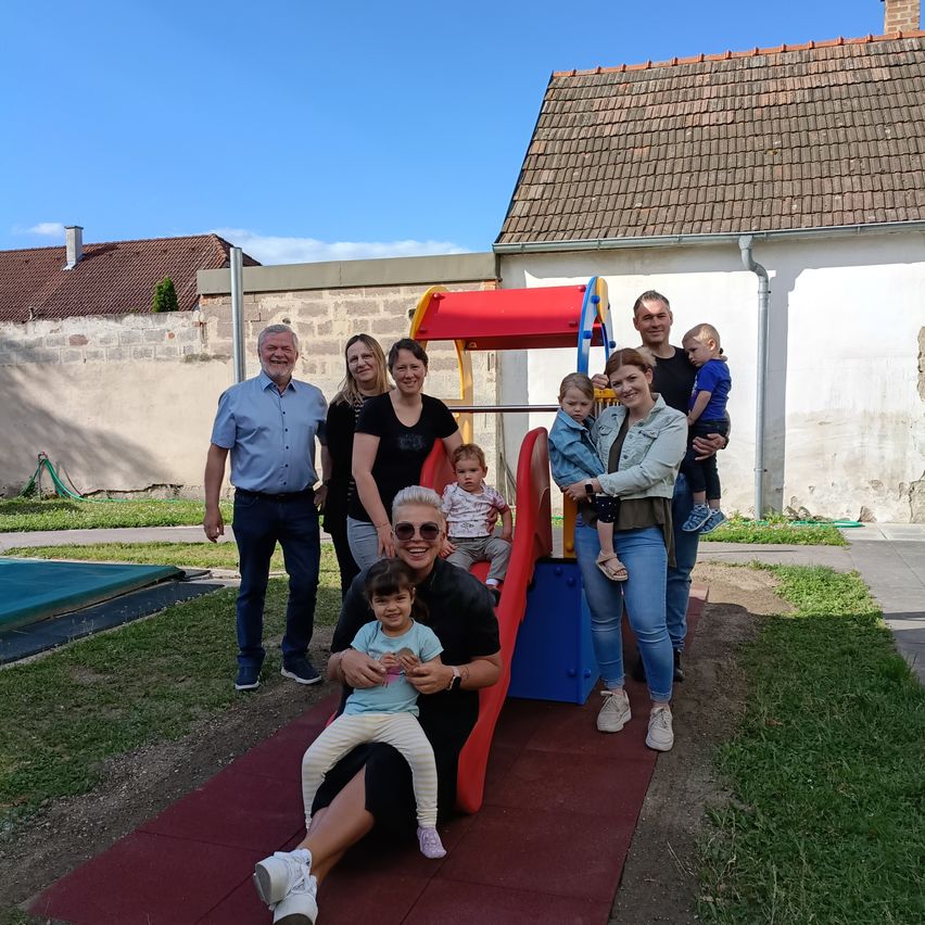 Eine Familie mit mehreren Kindern steht in einem Hof mit einem Spielplatz im Hintergrund. Sie lächeln und posieren für ein Foto.