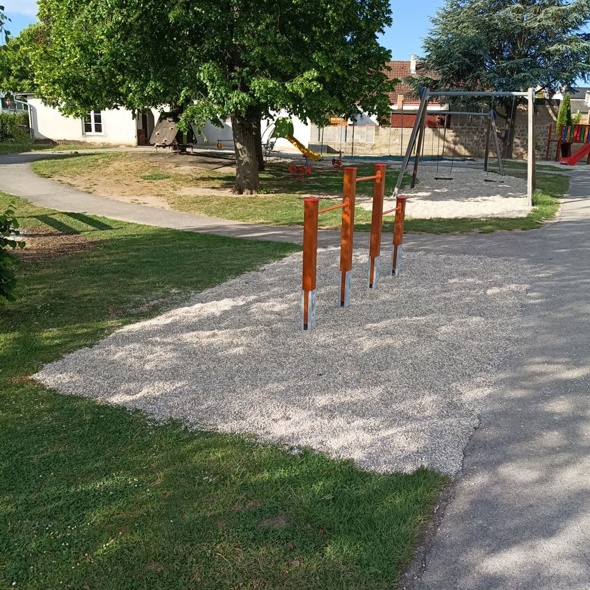 Spielplatz im Freien mit Kiesfläche, Schaukel und roter Rutsche an einem sonnigen Tag.