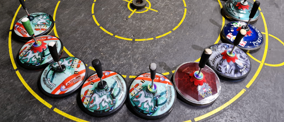 Ein kreisförmiges Spiel mit gelben Linien, das mehrere kreisförmige Objekte mit verschiedenen Designs und Farben aufweist. Die Objekte haben Griffe und sind in einem kreisförmigen Muster auf einem grauen Boden platziert.