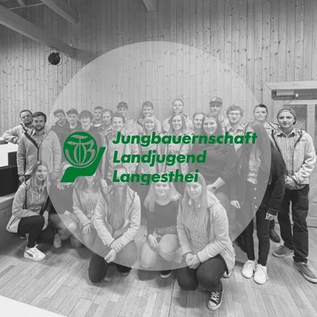 Eine Gruppe junger Landwirte und junger Landfrauen posiert für ein Foto in einem Raum mit Holzwänden. Sie lächeln und scheinen Teil einer Organisation zu sein.