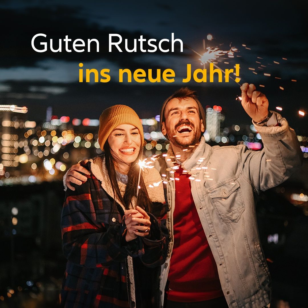 Zwei Personen feiern Silvester mit Feuerwerk, lächeln und halten Händchen vor einer nächtlichen Stadtsilhouette.