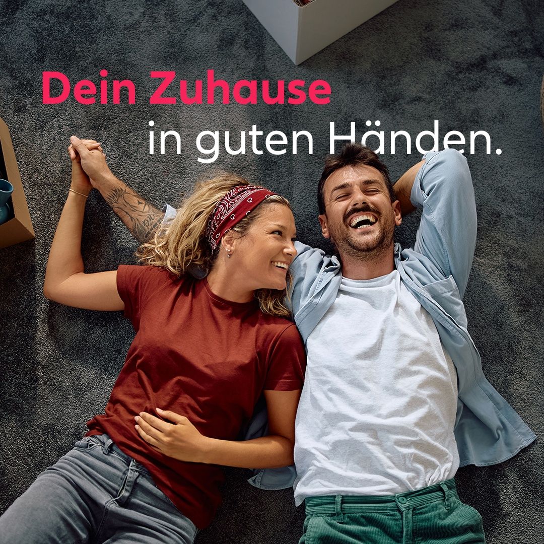 Ein Paar liegt mit einem lächelnden Mann auf dem Boden, die Frau umarmt ihren Partner. Der Text darüber lautet 'Dein Zuhaus in guten Handen'. Die Umgebung deutet auf eine entspannte und glückliche Wohnatmosphäre hin.