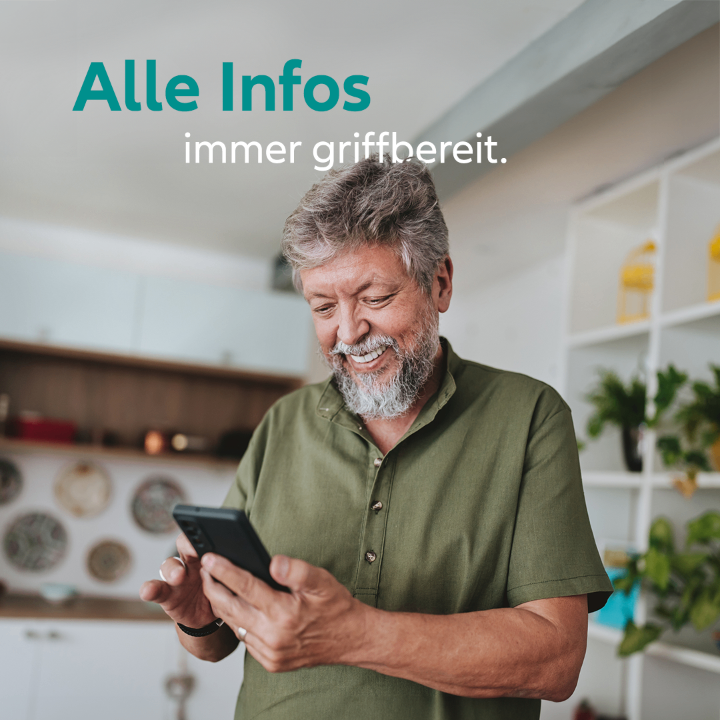 An older man wearing a green shirt is looking at his smartphone, smiling in the kitchen. The text reads, 'Alle Infos immer griffbereit'.