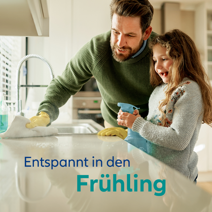 Ein Vater und seine Tochter putzen die Küche. Sie tragen beide Handschuhe und lächeln. Der Vater hält ein Tuch und die Tochter eine Flasche. Die Bildunterschrift lautet 'Entspannt im Frühling'.