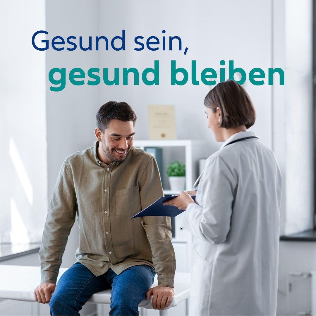 Ein lächelnder Mann sitzt auf einem medizinischen Untersuchungstisch und schaut einer Ärztin ins Gesicht, die eine Mappe und einen Stift in der Hand hält. Der Text 'Gesund sein, gesund bleiben' ist über ihnen prominent angezeigt.