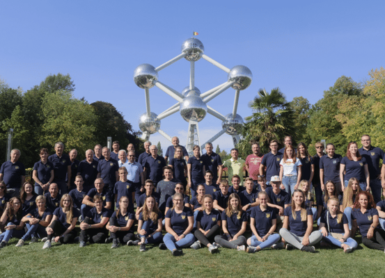 Eine Gruppe von Menschen in blauen Hemden posiert für ein Foto vor dem Atomium in Brüssel.