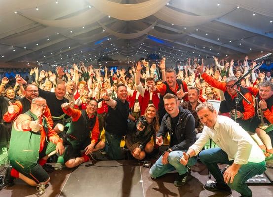 Eine Gruppe von Menschen, einschließlich Musiker, posiert für ein Foto auf einer Bühne mit einer Menge im Hintergrund.