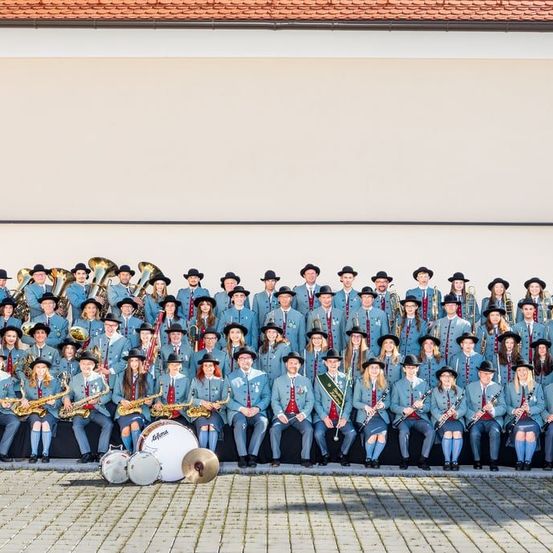 Eine Gruppe von Menschen in Uniformen und Hüten, die sitzen und stehen, Musikinstrumente halten und für ein Foto vor einem Gebäude posieren.