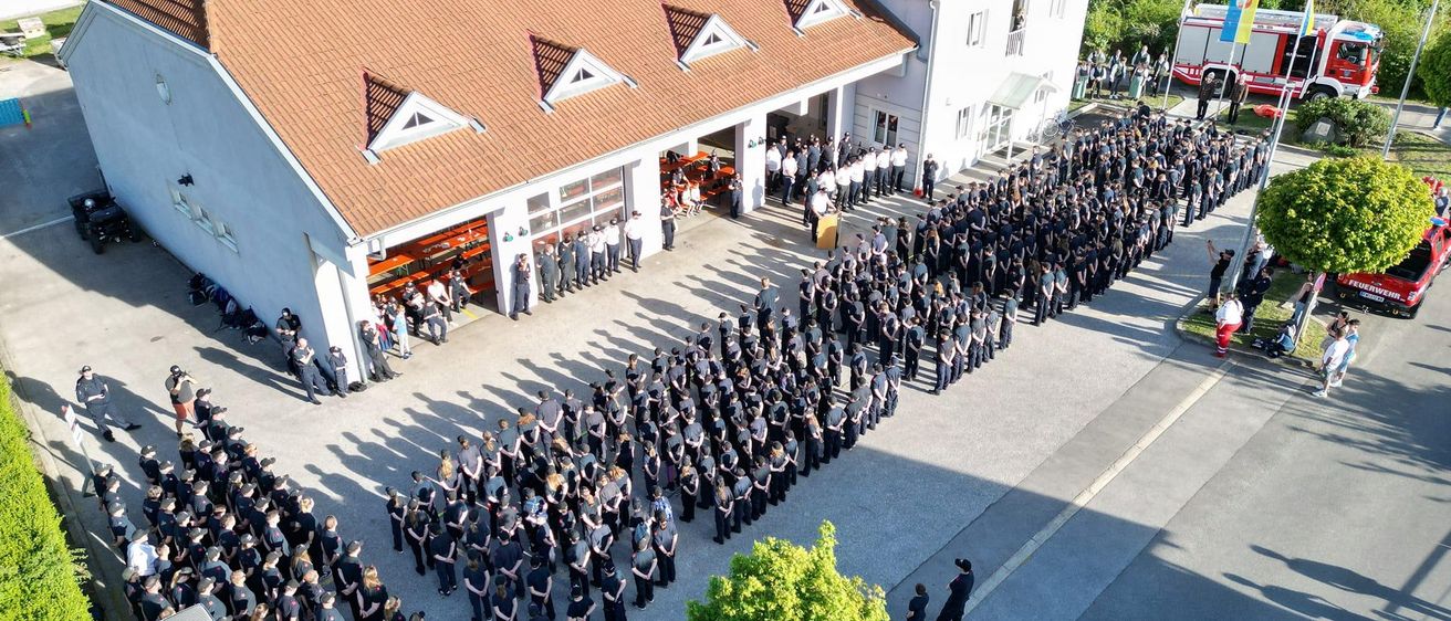 Eine Draufsicht auf eine große Gruppe von Menschen in Uniform, die in Reihen vor einer Feuerwache stehen.