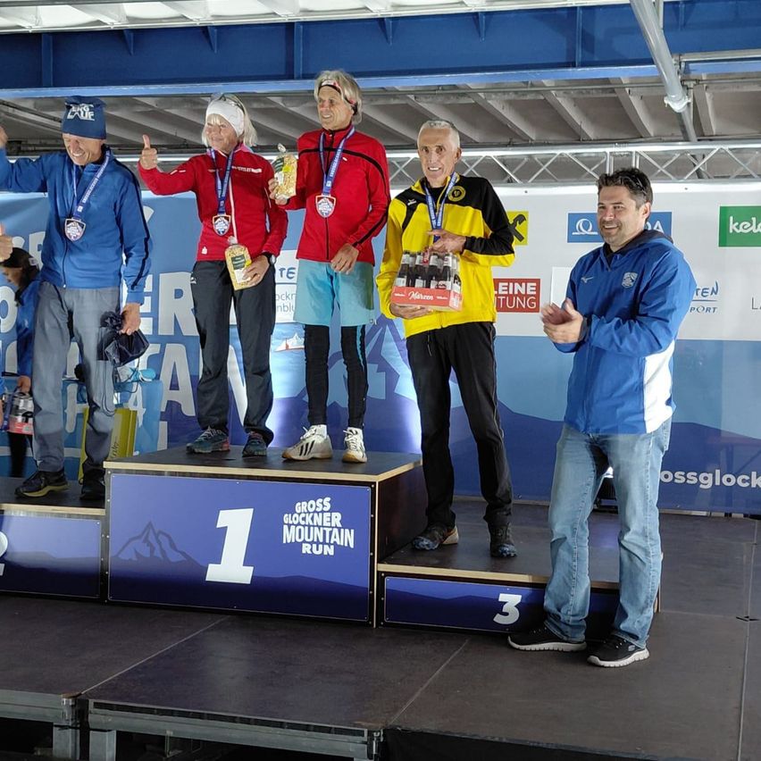 Fünf Personen stehen auf einem Podium für den Großglockner-Berglauf, mit Medaillen um den Hals. Das Podium ist mit 1, 2 und 3 gekennzeichnet.