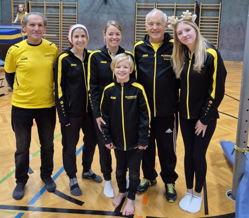 Eine Gruppe von Menschen in passenden gelben und schwarzen Sporttrikots mit Jako darauf posiert für ein Foto auf einem Basketballplatz.