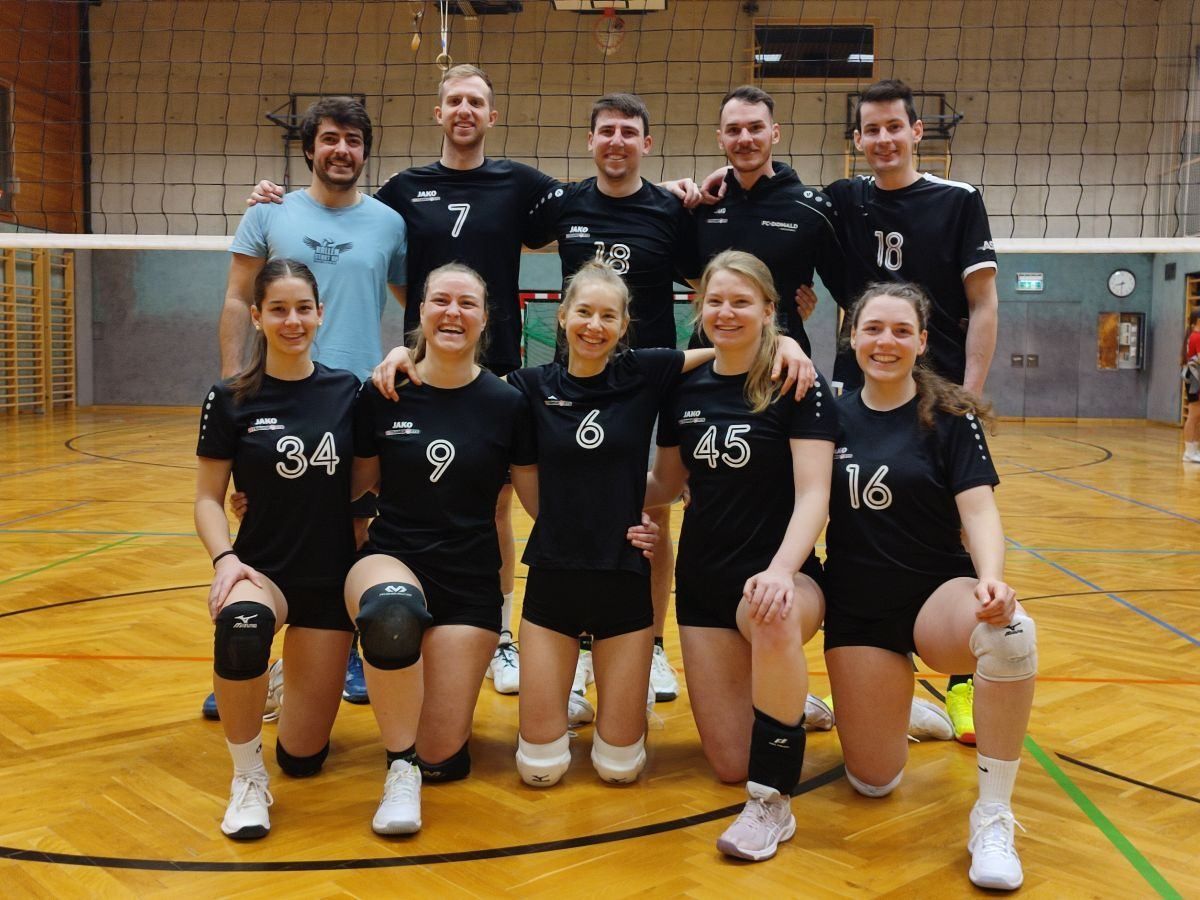 A volleyball team poses for a photo with numbers on their jerseys in a gym.