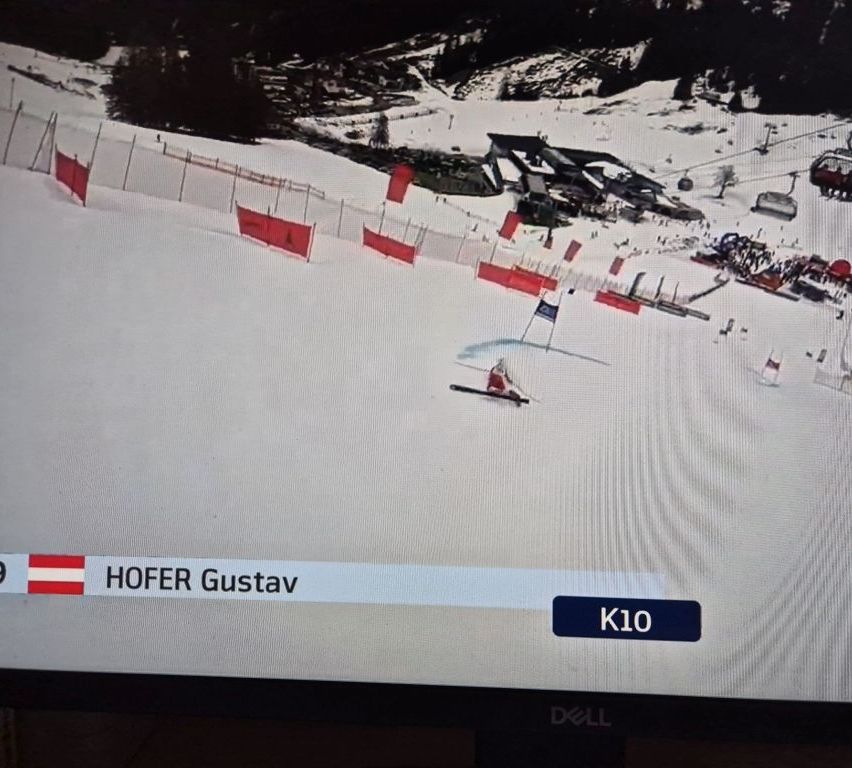 Ein Skifahrer fährt einen verschneiten Hang hinunter, gekennzeichnet mit dem Namen Hofer Gustav und der Nummer 10. Der Bildschirm ist auf einem Dell-Monitor.