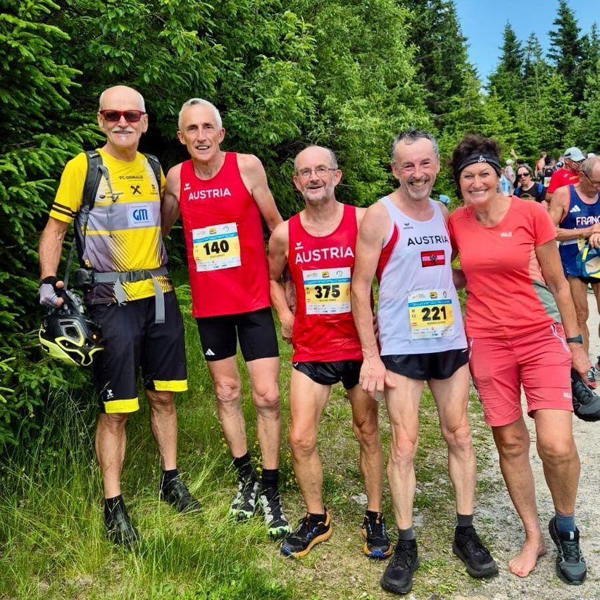 Vier Personen in Sportkleidung posieren für ein Foto auf einem Weg. Sie haben Nummern auf ihren Trikots, 140, 375 und 221. Sie lächeln und scheinen bei einem Marathon zu sein.