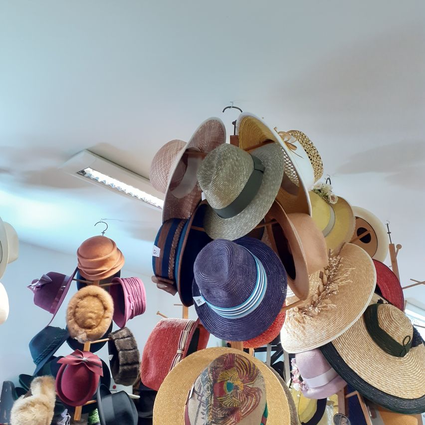 Eine Sammlung verschiedener Hüte hängt von der Decke, darunter Stroh-, Filz- und Pelzhüte, alle an Haken aufgehängt.