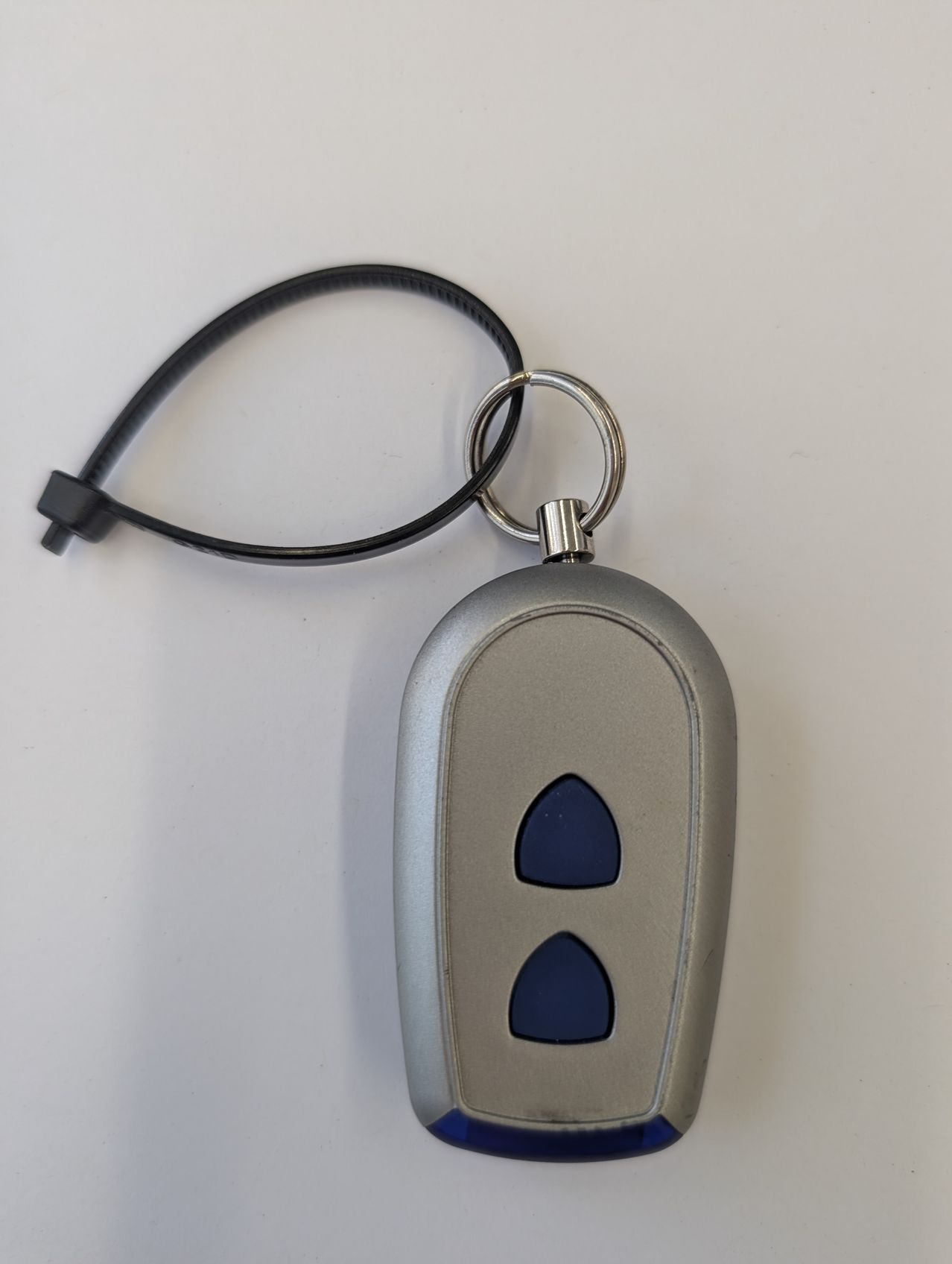 Ein silberner Schlüsselbund mit einem schwarzen Gurt. Der Schlüsselbund hat eine runde Form mit zwei blauen dreieckigen Tasten.