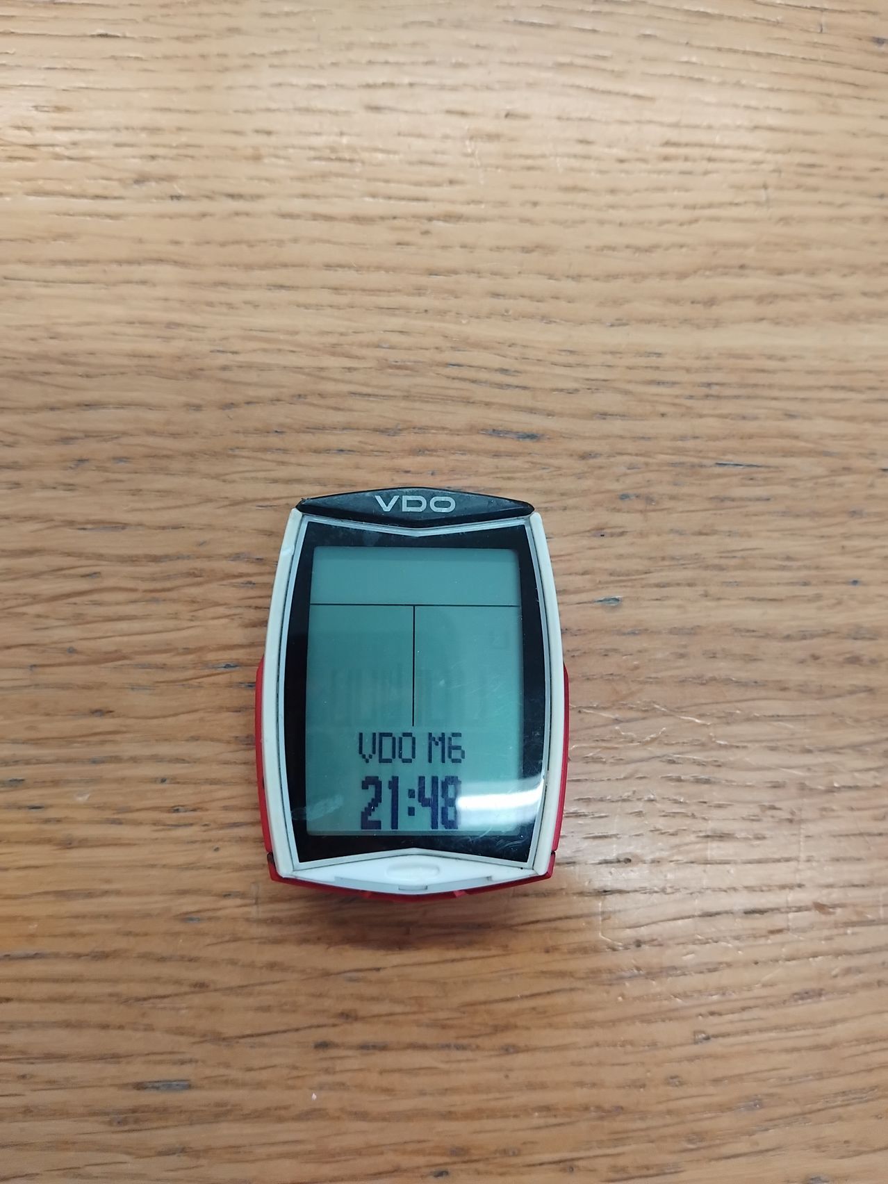 Ein rot-weißes VO2 Max Fahrradcomputer zeigt 'VO2 Max 16 21:48' auf einer Holzoberfläche an.