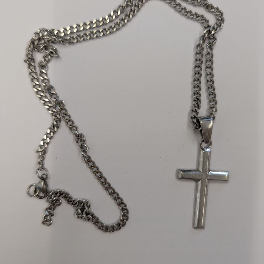 Ein silbernes Kreuz-Anhänger an einer silbernen Kette, auf einem weißen Hintergrund dargestellt.