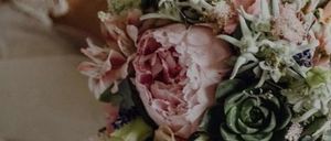 Eine Braut hält einen Blumenstrauß mit einer Mischung aus rosa, pfirsichfarbenen und grünen Blumen und Sukkulenten.