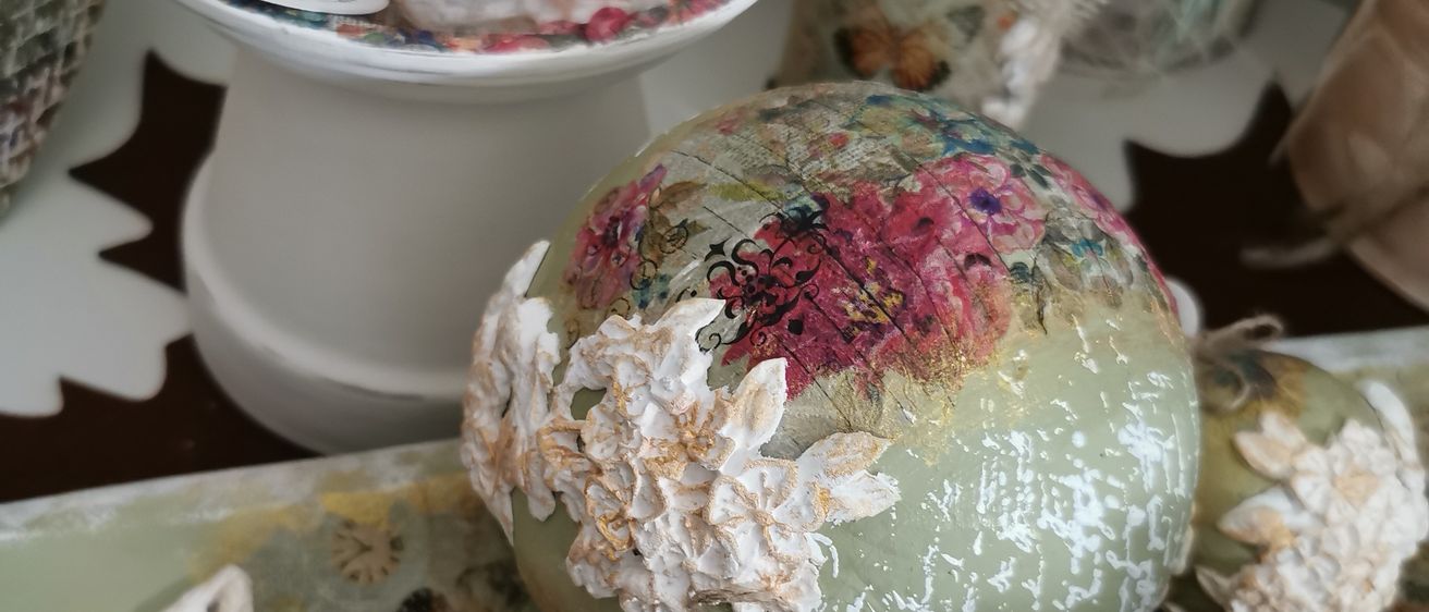 Eine dekorative Anzeige mit einer Kerze auf einem weißen Teller, Blumendekorationen und einem Ei mit weißen Blumen und einem Etikett.