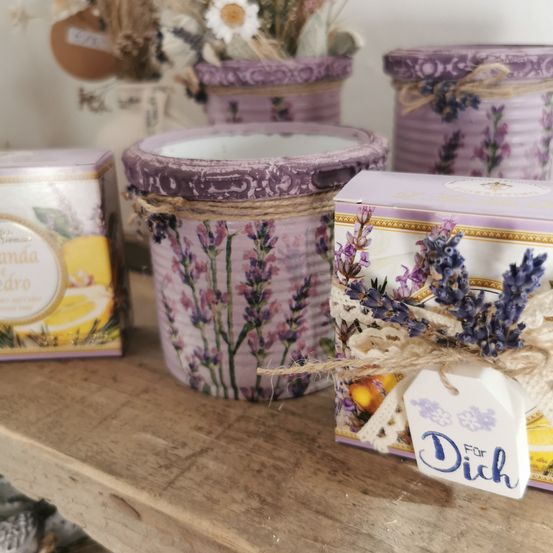 Ein Holzregal hält mehrere dekorative Gegenstände. Eine lila Box mit einem Lavendel-Tag lautet Für Dich. Andere Gegenstände umfassen eine Blechdose mit Lavendeldesign und eine weiße Box mit Zitronendesign.