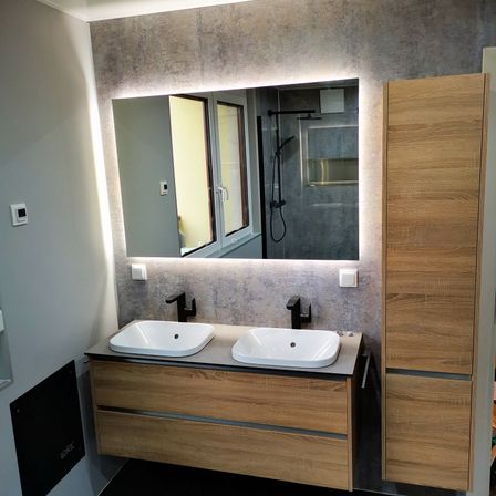 Ein modernes Badezimmer mit zwei weißen Waschbecken, einem großen Spiegel und Holzschränken. Die Wand hat eine graue Textur und die Armaturen sind schwarz.