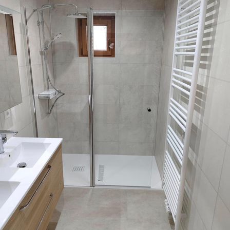 Ein Badezimmer mit Dusche, Waschbecken und einem Holzschrank. Der Duschbereich ist mit grauen Fliesen gefliest, und die Wände sind ebenfalls gefliest.