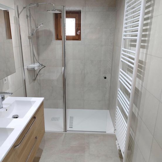 Ein Badezimmer mit Dusche, Waschbecken und einem Holzschrank. Der Duschbereich ist mit grauen Fliesen gefliest, und die Wände sind ebenfalls gefliest.