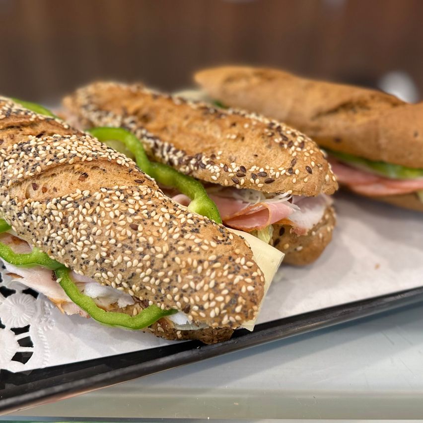 Drei Sandwiches auf einem Tablett, mit Sesam bestreut, enthalten Scheiben von grüner Paprika, Schinken und Käse.