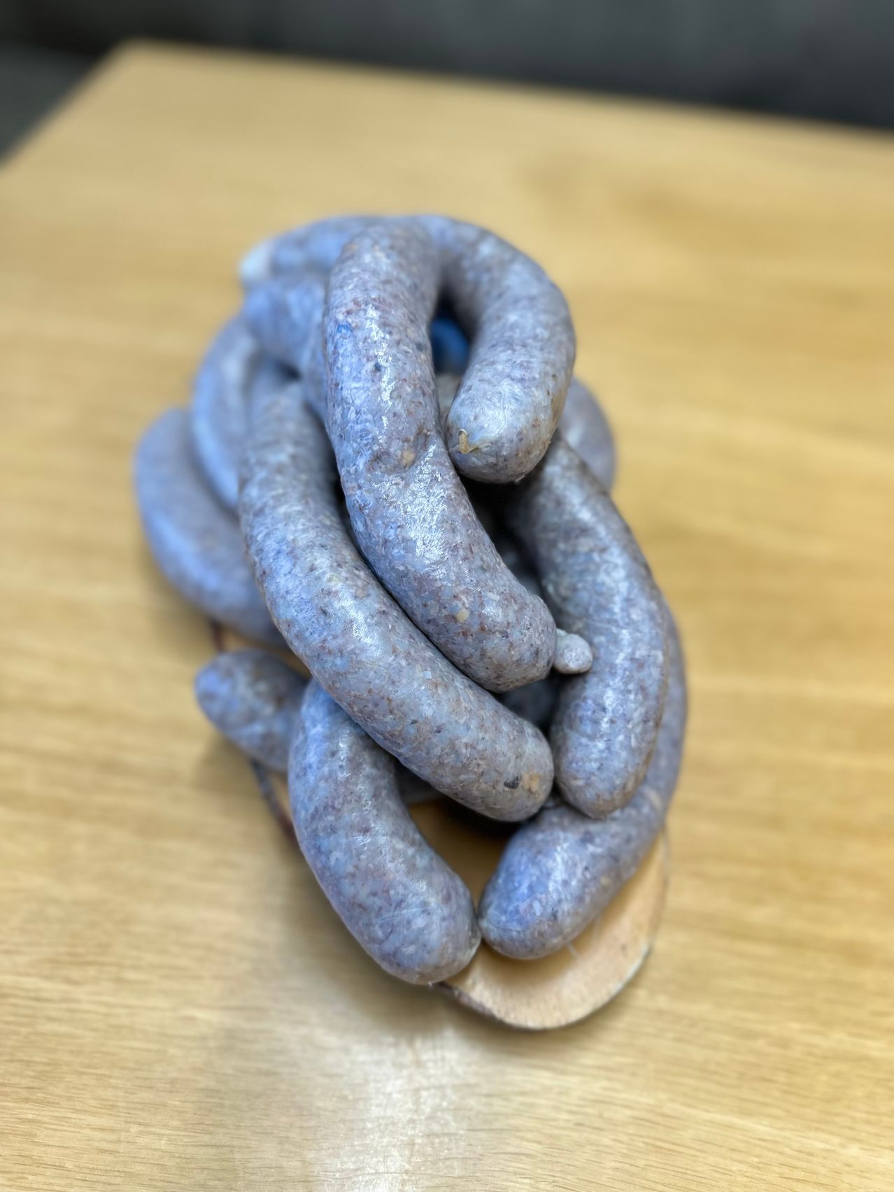 Eine Nahaufnahme eines Haufens blauer Würste auf einem Holzlöffel, der auf einem Holztisch liegt. Die Würste sind eng aufgerollt und haben ein rustikales Aussehen.