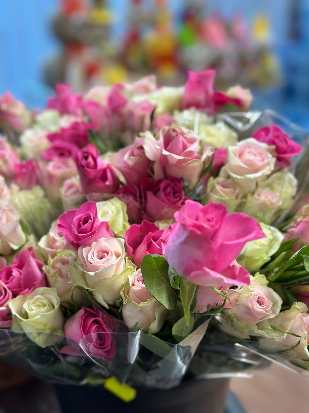 A close-up view of a bouquet of pink and white roses with green leaves, possibly in a flower shop. The roses are arranged in a neat, orderly fashion.