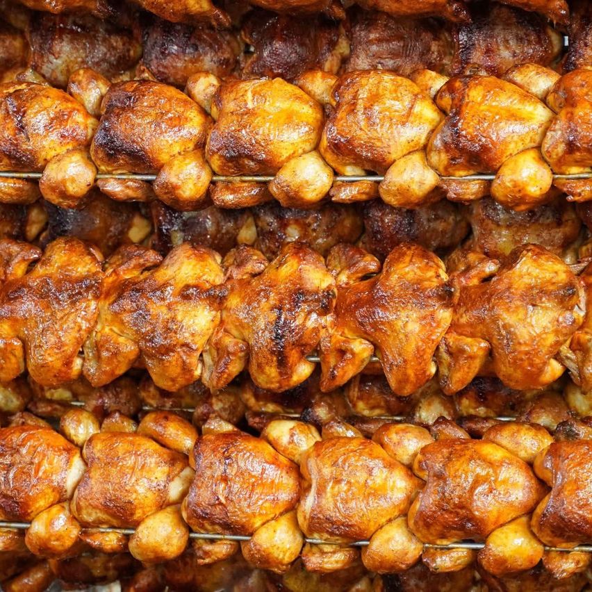 Multiple rows of whole, roasted chickens are displayed on racks, showing a golden-brown color and crispy skin.