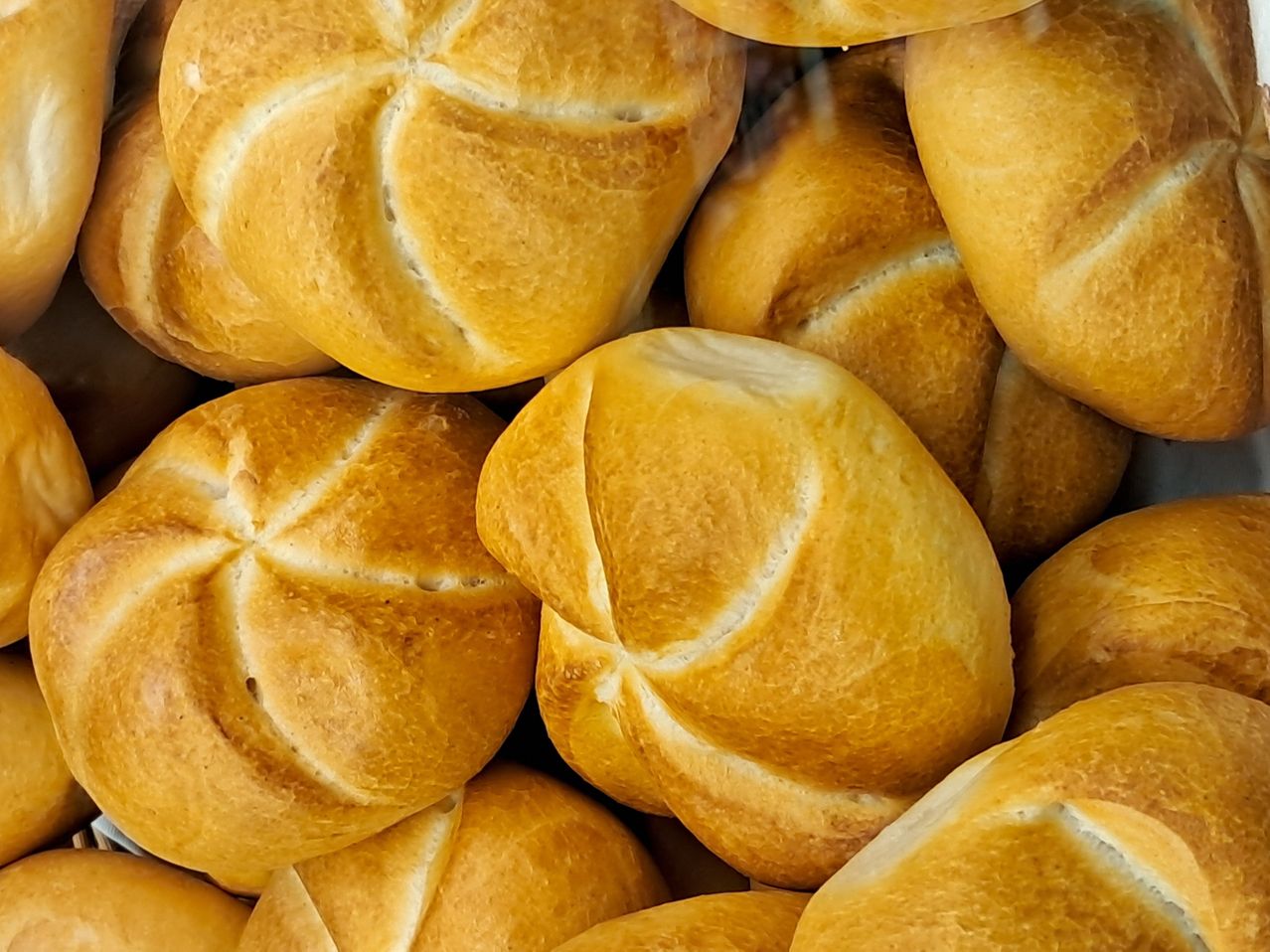 Ein Nahaufnahme von mehreren goldbraunen Brezeln mit kreuzförmigen Schnitten auf ihrer Kruste. Die Brezeln sind ordentlich gestapelt und zeigen ihre Textur und goldene Farbe.