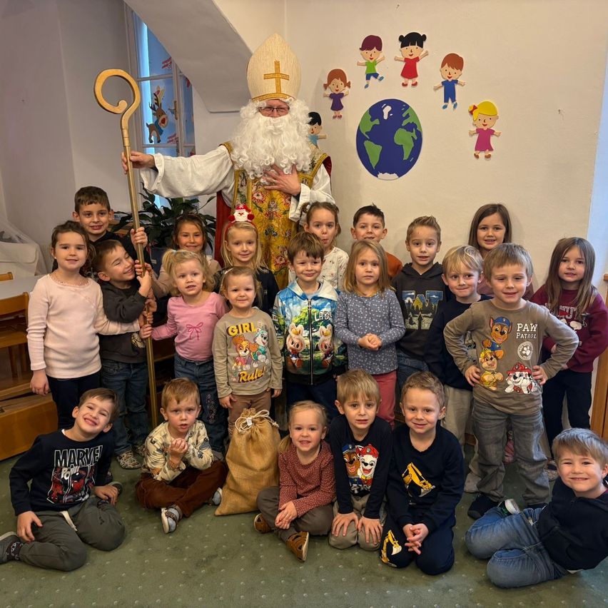 Eine Gruppe von Kindern mit einer als Weihnachtsmann verkleideten Person posiert für ein Foto in einem Raum.